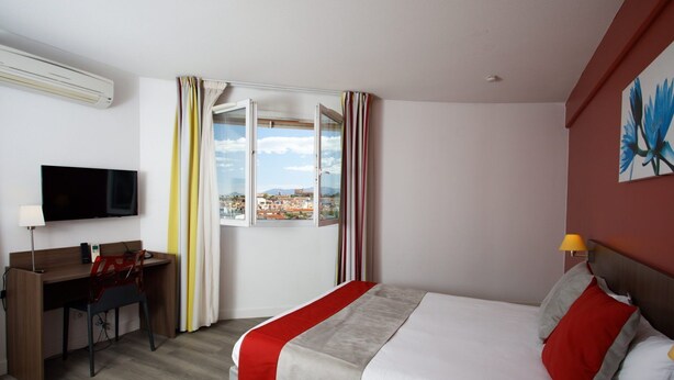 Une chambre d’hôtel équipée d’un lit, d’un bureau, d’une chaise, d’une télévision et d’une fenêtre avec des rideaux.