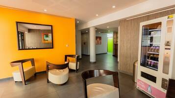 Un hall d’hôtel avec un mur orange vif, un distributeur automatique et des sièges modernes.