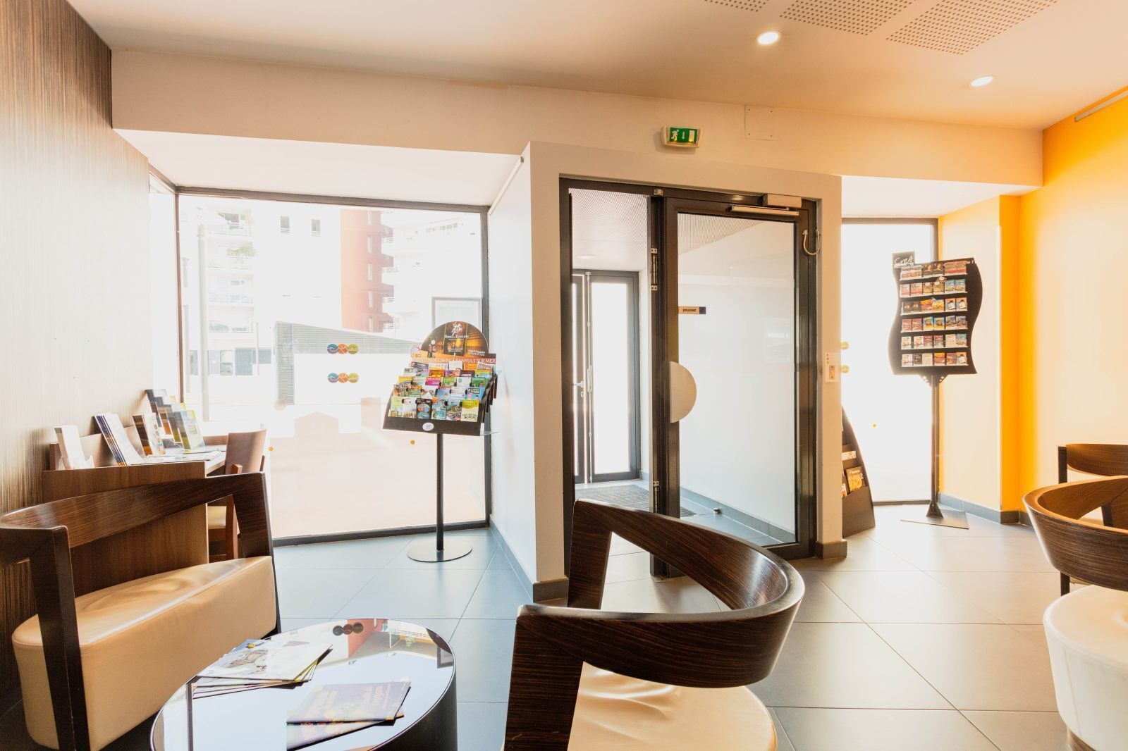 Een hotel lobby met zitplaatsen, een receptiebalie, een glazen deuropening en een tijdschriftenrek.