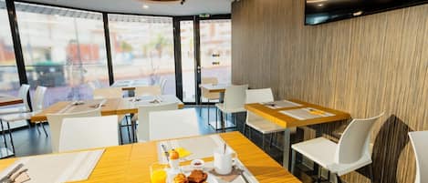 Un espace repas moderne avec des tables et des chaises, des articles pour le petit-déjeuner et de grandes fenêtres.