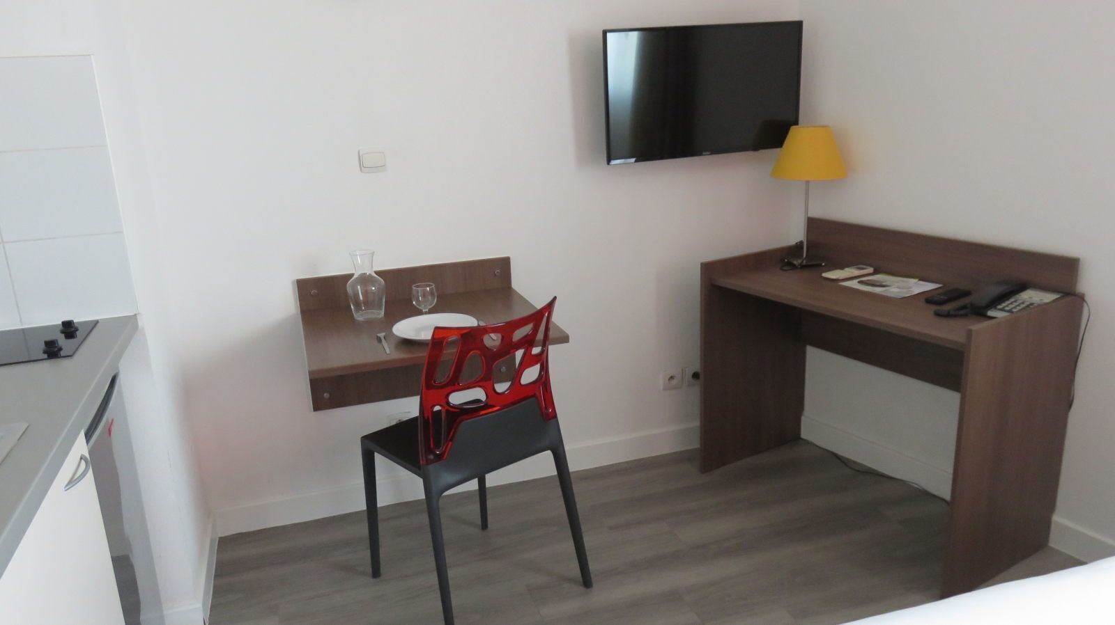 Ein Hotelzimmer mit Schreibtisch, Stuhl, Wand-Fernseher, Nachttisch mit Lampe und Bett.