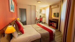 A hotel room with a bed, bedside lamps, a desk, a chair, a television, and a kitchenette.