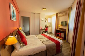 Une chambre d’hôtel équipée d’un lit, de lampes de chevet, d’un bureau, d’une chaise, d’une télévision et d’une kitchenette.
