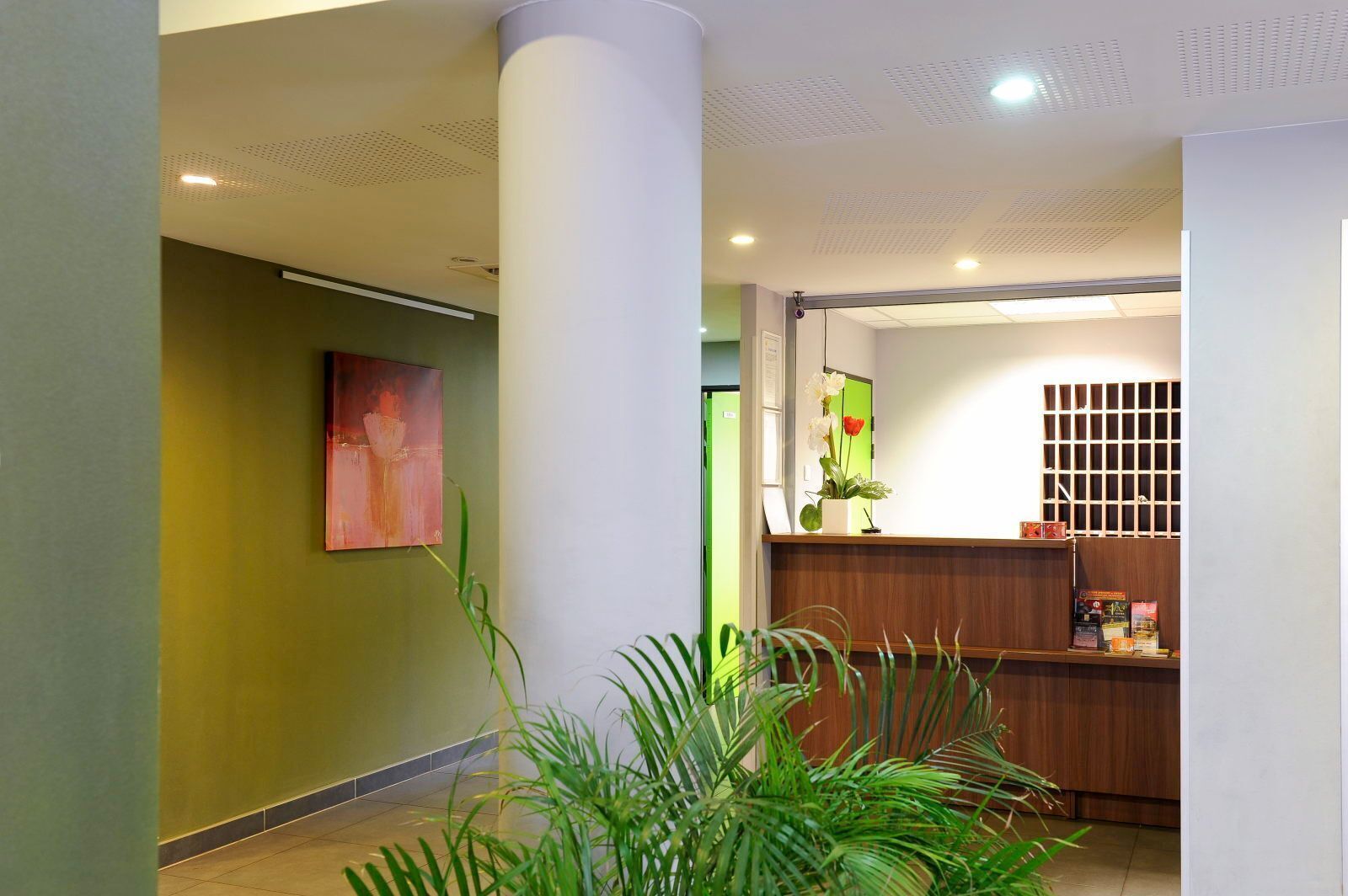 A reception area with a wooden reception desk, a green wall, and a large column.