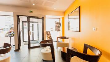A reception area with a modern design, featuring a bright yellow wall, a reception desk, and a seating area with chairs and a small table.