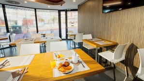 A modern dining area with tables and chairs, breakfast items, and large windows.