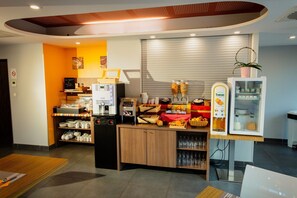 A breakfast area with a coffee machine, a refrigerator, and a variety of food items.