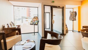 A hotel lobby with seating, a reception desk, a glass door entrance, and a magazine rack.