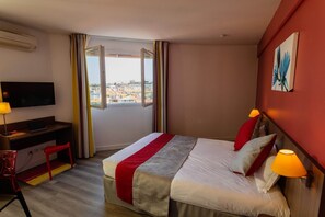 A hotel room with a bed, desk, chair, TV, and a window with curtains.
