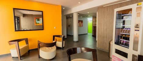 A hotel lobby with a bright orange wall, a vending machine, and modern seating.
