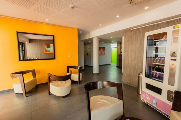 Un hall d’hôtel avec un mur orange vif, un distributeur automatique et des sièges modernes.