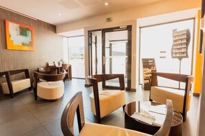 Un hall d’hôtel moderne comprenant un comptoir d’accueil, un espace salon et une vue sur la rue.