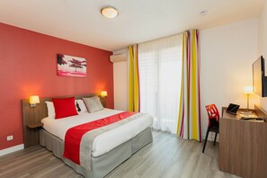 A hotel room with a bed, bedside lamps, a desk with a laptop, a chair, and a TV.