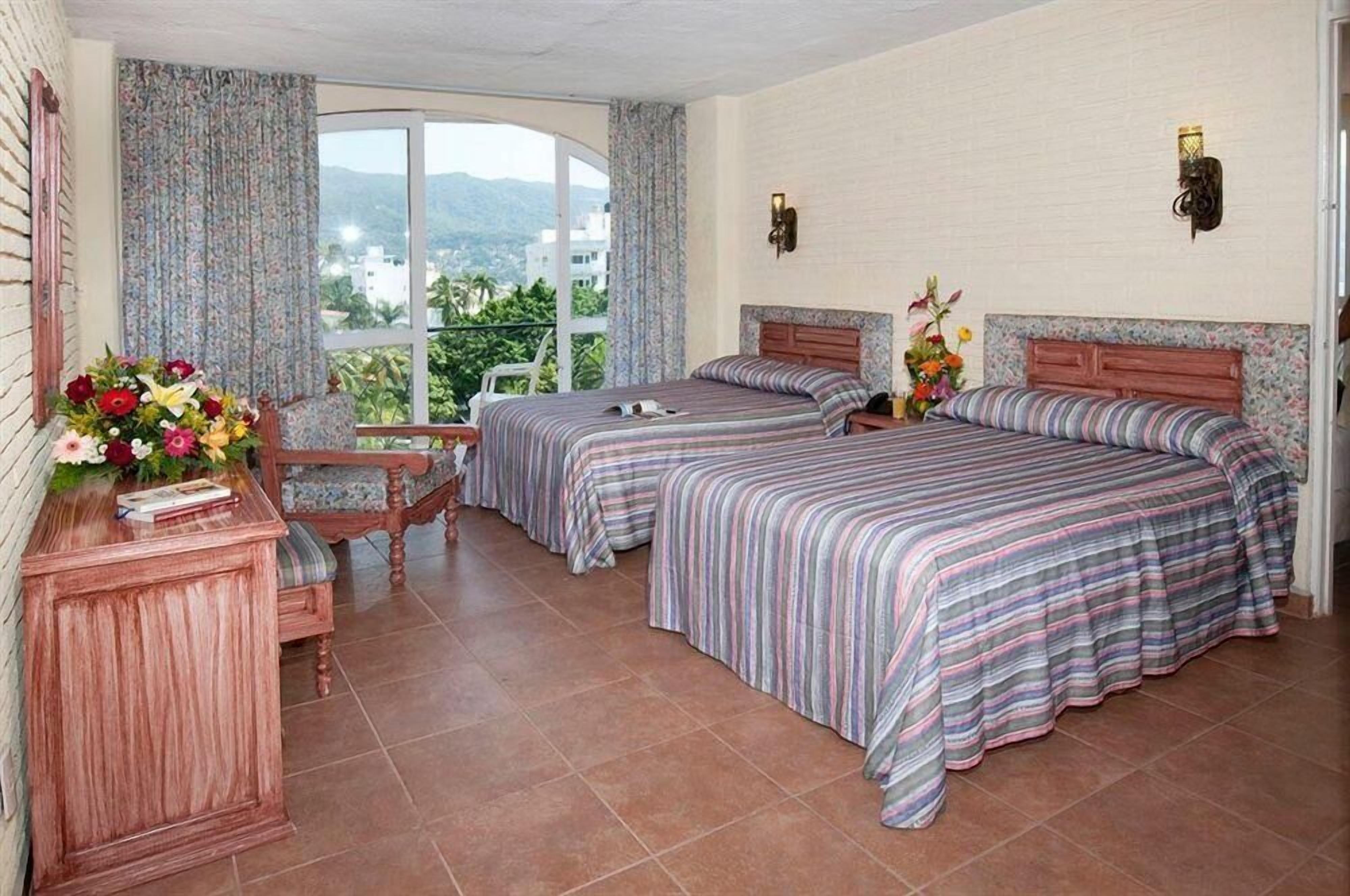 A hotel room with two beds, a wooden desk, and a view of the outdoors.
