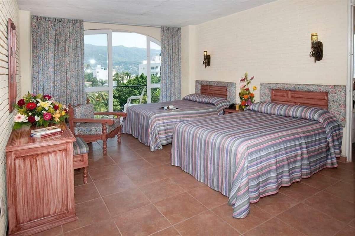 Habitación de hotel con dos camas, un escritorio de madera y vistas al exterior.