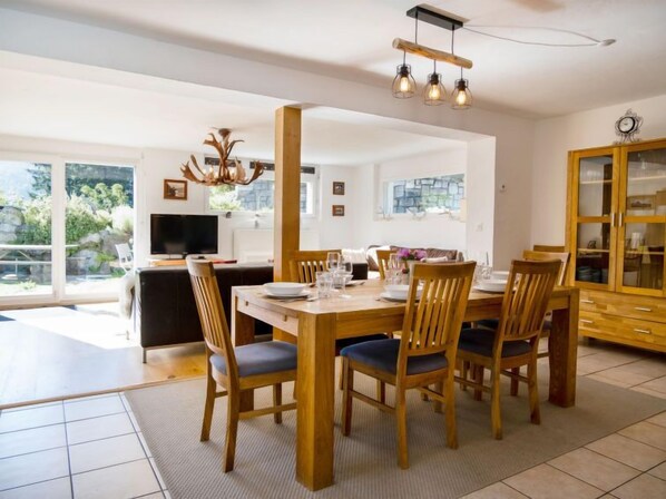 Un comedor moderno con una mesa y sillas de madera, un televisor y vistas a zonas verdes.