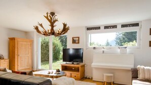 Een gezellige woonkamer met een groot raam, een houten kast, een televisie, een piano en een open haard.