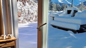 Een kamer met een houten kast en een glazen deur die uitkomt op een besneeuwd landschap met een bank.