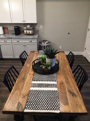 Una mesa de comedor de madera con un camino de mesa blanco y negro estampado, rodeada de sillas negras.