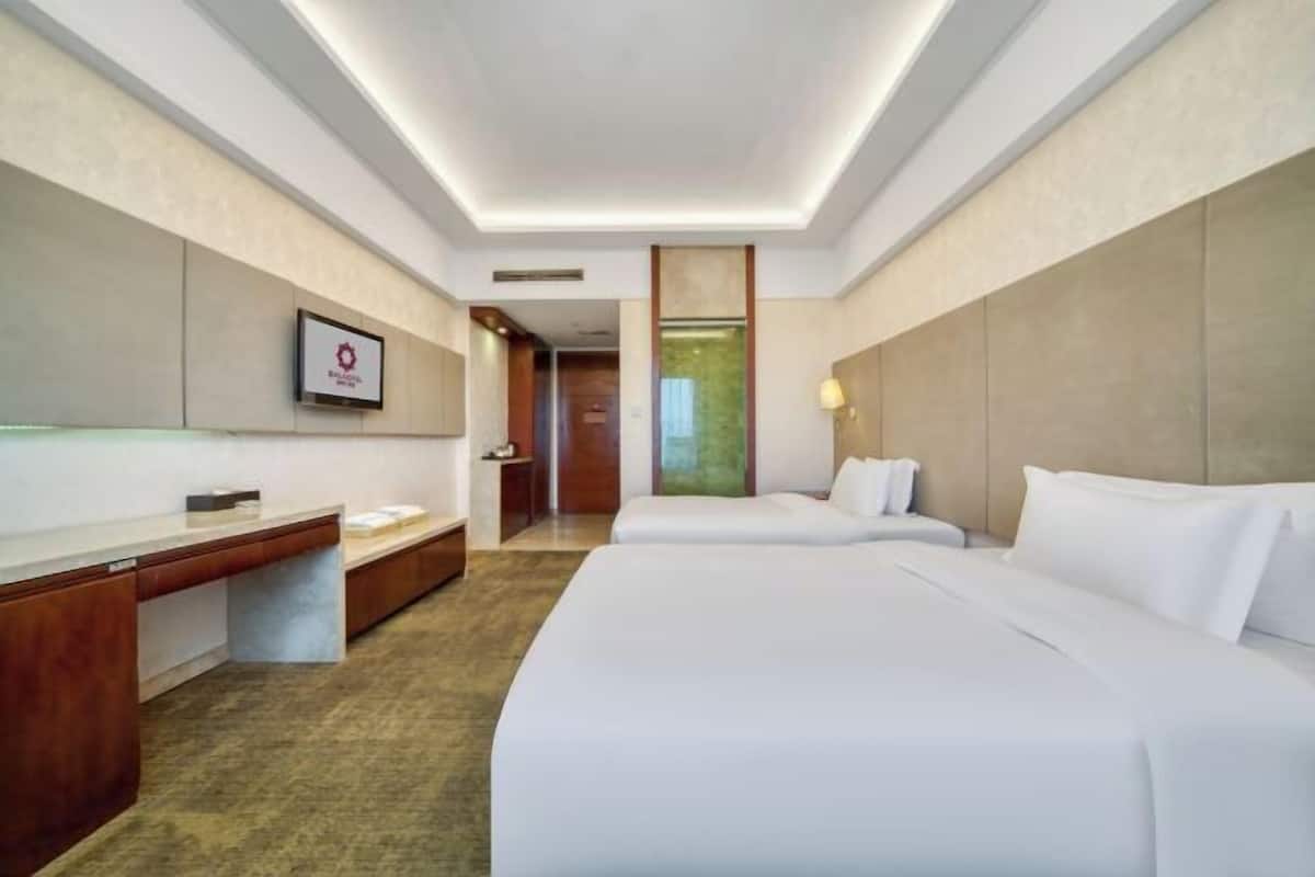 A hotel room with a large bed, a desk, and a chair. There is a framed picture on the wall and a window with a view of a building.