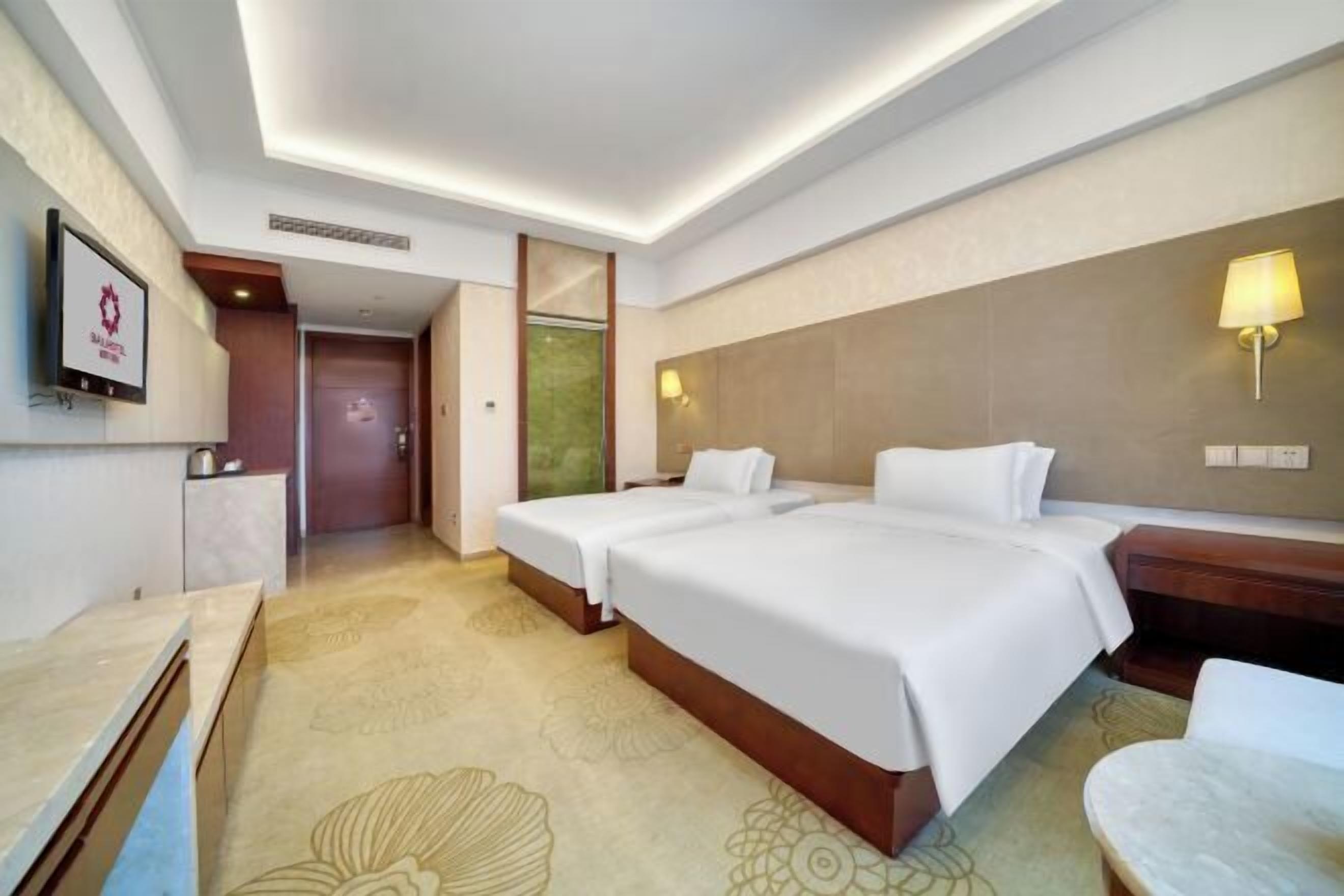 A hotel room with two beds, a desk, a chair, and a TV.