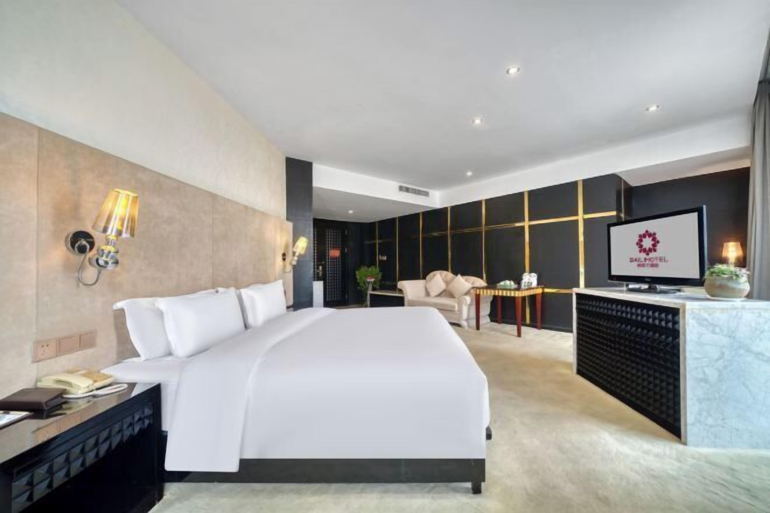Ett modernt hotellrum med en stor säng, ett skrivbord med en dator, en TV och en minibar.