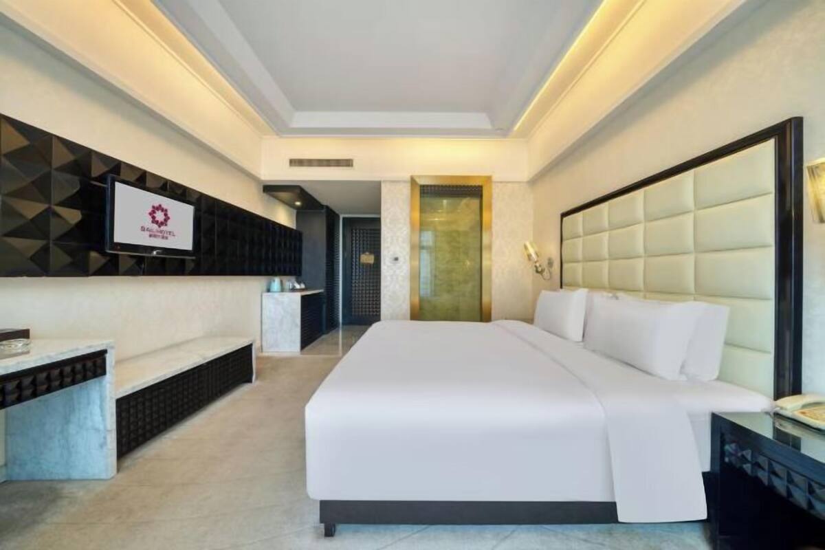 A hotel room with a large bed, a TV mounted on the wall, a desk, and a bench.