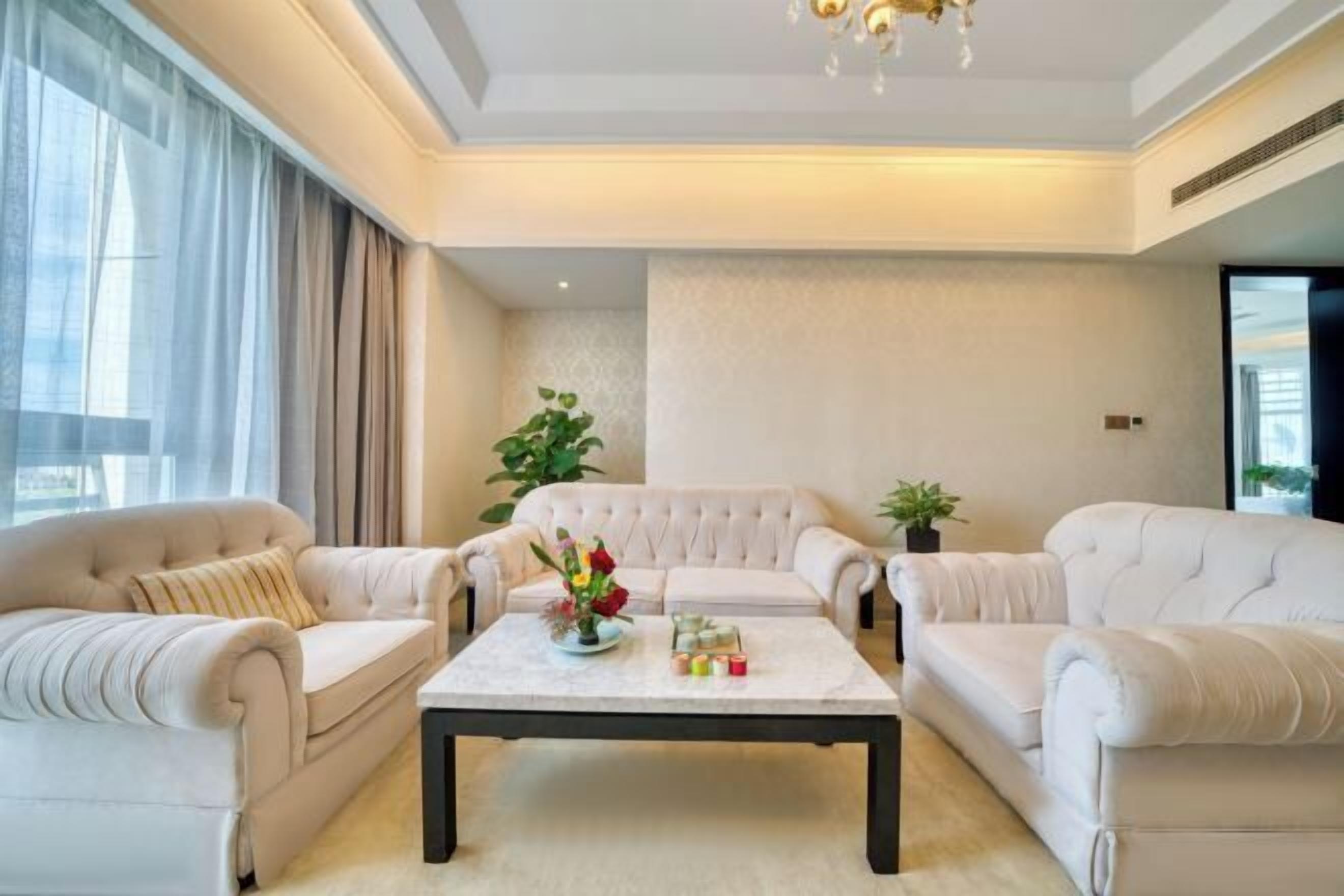 Una sala de estar moderna con un amplio sofá, una mesa de centro con adornos y un gran ventanal con cortinas.