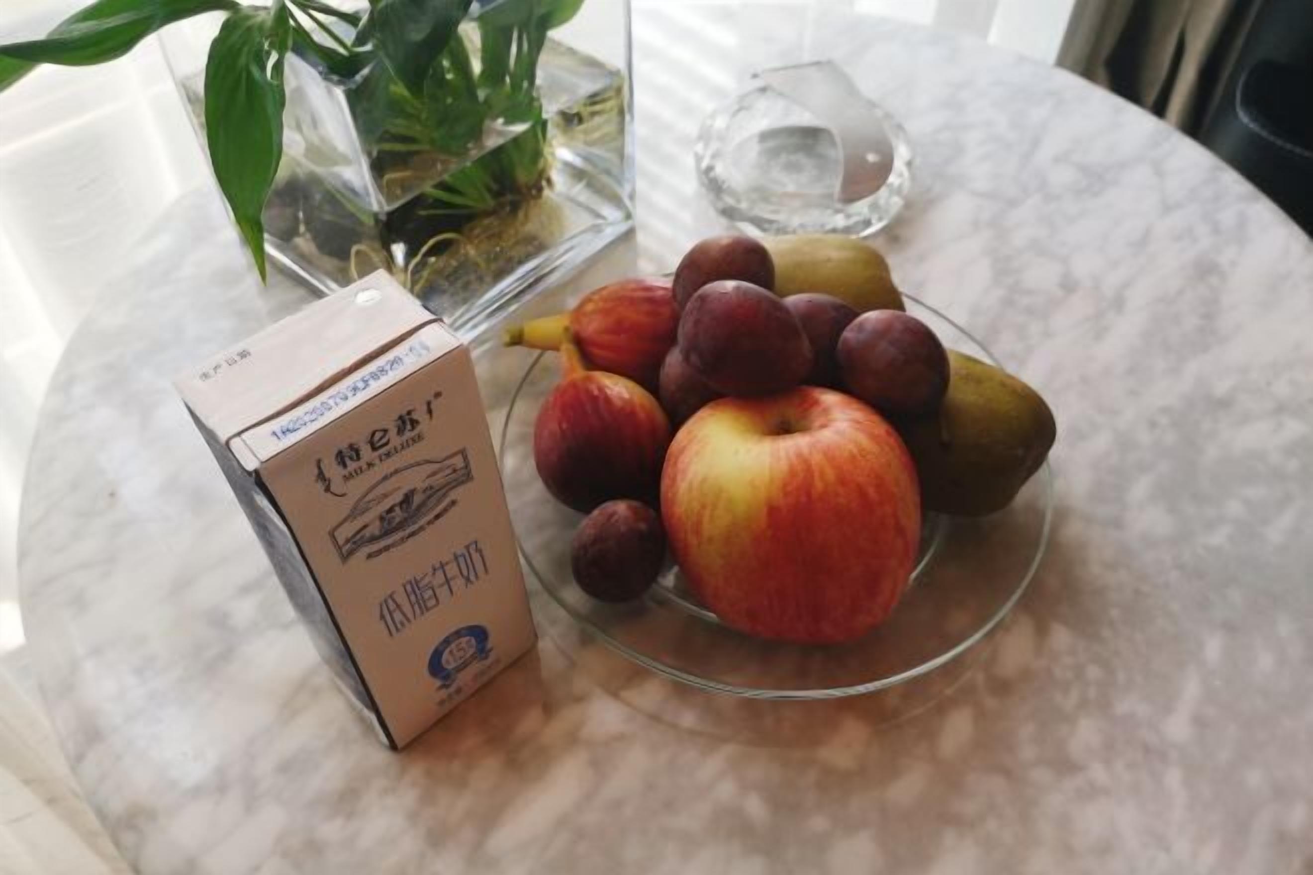 A marble table with a glass bowl containing apples and pears, a potted plant, and a clear glass.