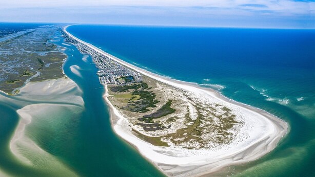 An aerial view of a coastal area with a long, narrow beach, a small peninsula with buildings, and a clear blue ocean. - Waterfront South End Serenity! Bring your boat and your pup, leave the linens!
 (Holly Ridge)