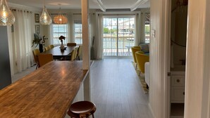 A modern dining area with a long wooden table, yellow chairs, and hanging pendant lights. - Waterfront South End Serenity! Bring your boat and your pup, leave the linens!
 (Holly Ridge)