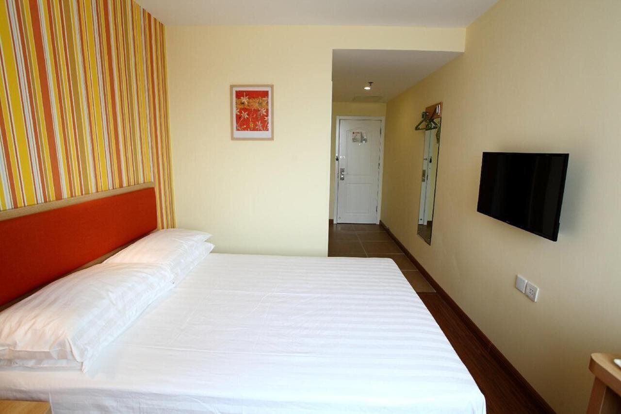 A hotel room with a bed, a television mounted on the wall, and a door leading to another room.