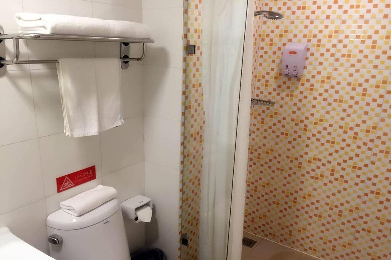 A bathroom with a toilet, a towel rack, a shower with a glass door, and a soap dispenser.