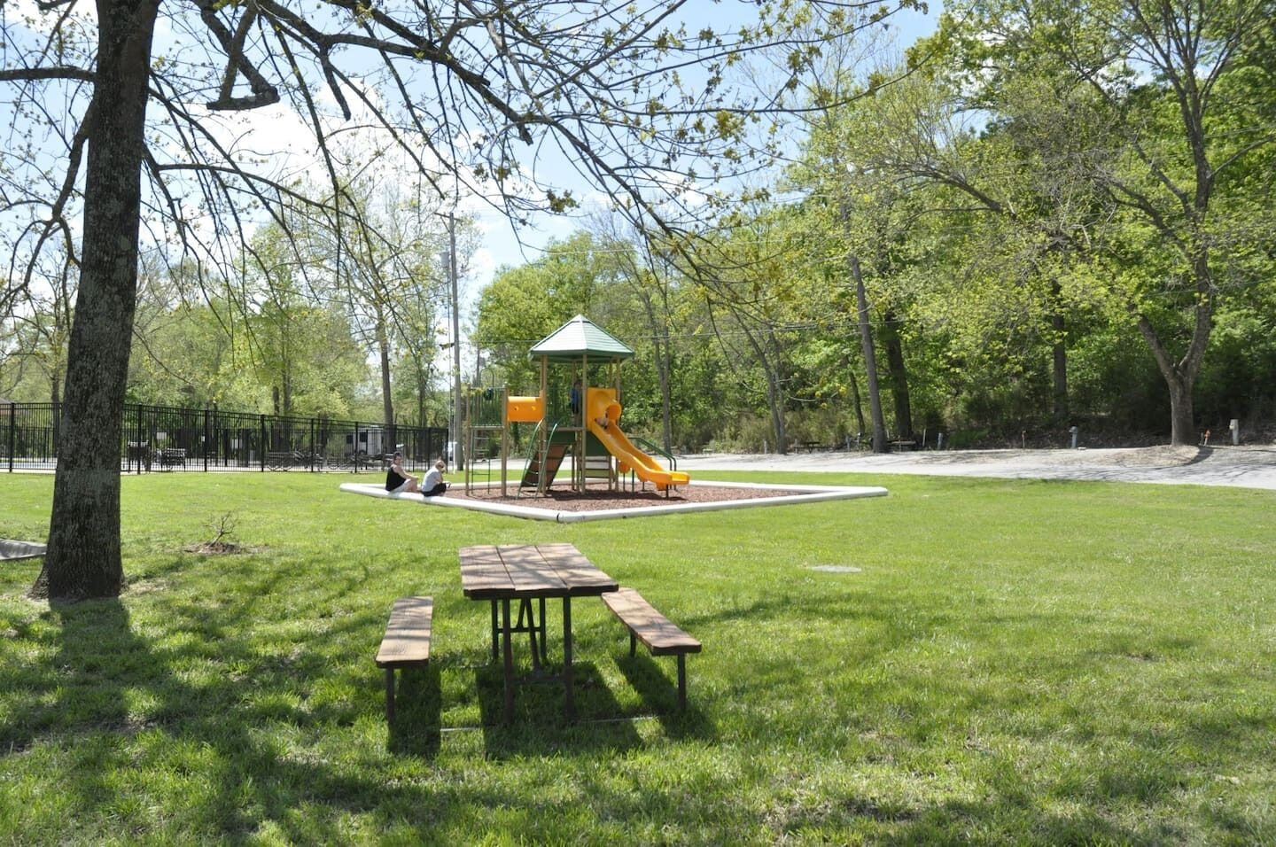 Un parque con un área de juegos que incluye un tobogán, una estructura de juegos con techo verde y mesas de picnic.