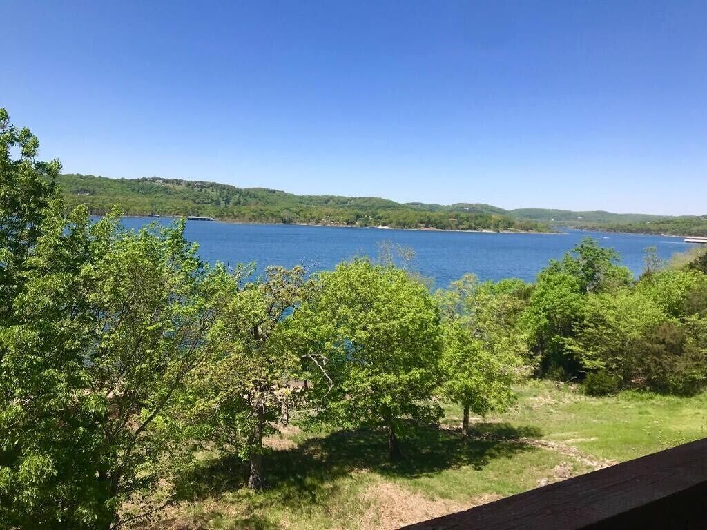Vista de un lago con árboles en primer plano y colinas al fondo.