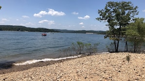 Vista para o lago com margem rochosa, árvores e barcos na água.