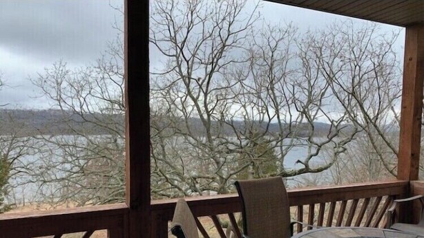 Área externa coberta com mesa e cadeiras, com vista para a água e árvores.