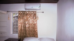 A bedroom with a bed, a window with a curtain, a nightstand, and an air conditioning unit.