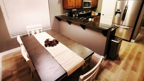 Moderni keittiö, jossa on puiset kaapit, ruostumattomasta teräksestä valmistettu jääkaappi sekä ruokailutila, jossa on pöytä ja tuolit.