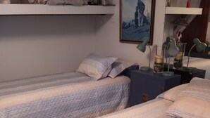 Dos llits individuals amb llençols combinats, una taula de nit amb una làmpada i una estant amb objectes decoratius.