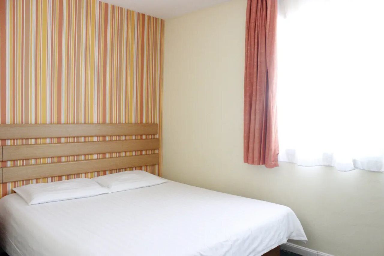 Una habitación de hotel con una pared a rayas, un cabecero de madera, una cama blanca y una ventana con cortina.