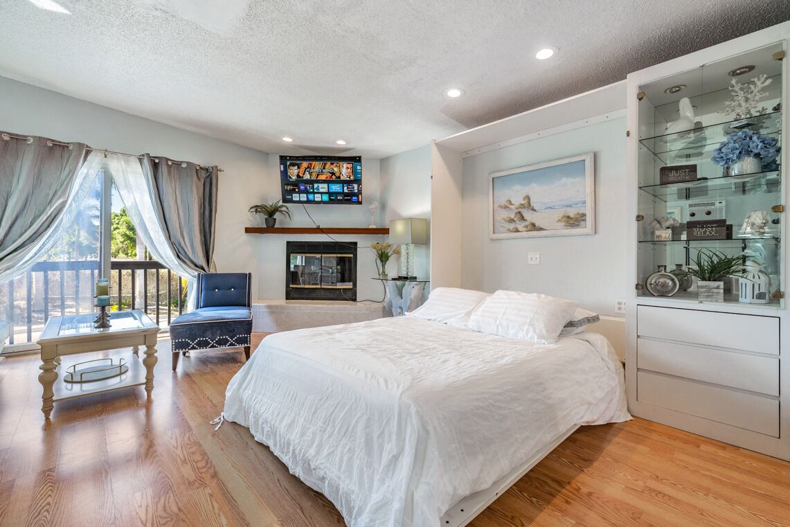 A bedroom with a large bed, a desk, a chair, a TV, and a glass cabinet with decorative items.