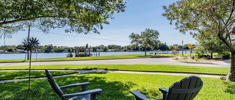 A park with two Adirondack chairs, a lake, and a walking path.