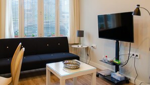 Moderni olohuone, jossa on musta sohva, lasinen sohvapöytä, televisio ja lamppu.