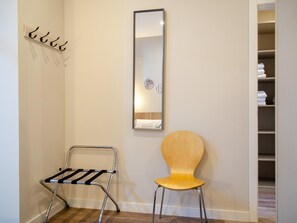 Simple, functional space with a metal drying rack, wooden chair, and large mirror.