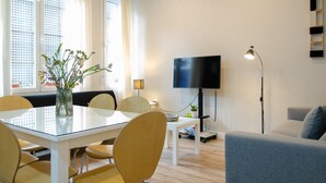 Una sala moderna con una mesa de comedor de vidrio, sillas amarillas, un sofá gris, un televisor de pantalla plana y una lámpara de pie.