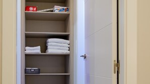 Un armario con repisas que contiene toallas dobladas, una caja roja y un control remoto.