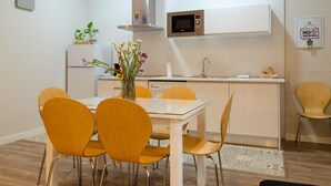 Una cocina moderna con armarios blancos, una campana extractora de acero inoxidable, microondas y un comedor con mesa blanca y sillas amarillas.