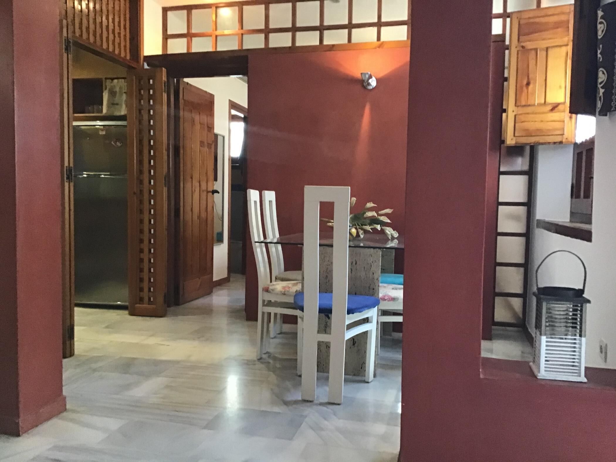 A dining area with a table and chairs, a refrigerator in the background, and a wooden partition.
