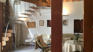 A spacious living area with a high ceiling, exposed wooden beams, a staircase, and a dining area with a table and chairs.